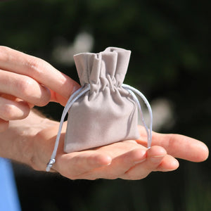 Grauer Geschenkbeutel für personalisierte Schlüsselanhänger, in zwei Händen gehalten.