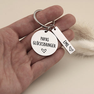 Papas Glücksbringer Schlüsselanhänger mit Namensanhänger in einer Hand als Größenvergleich.