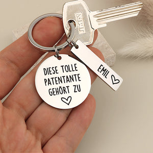 Größenvergleich des Schlüsselanhängers „Diese tolle Patentante gehört zu“ mit Namensanhänger Emil in der Hand.