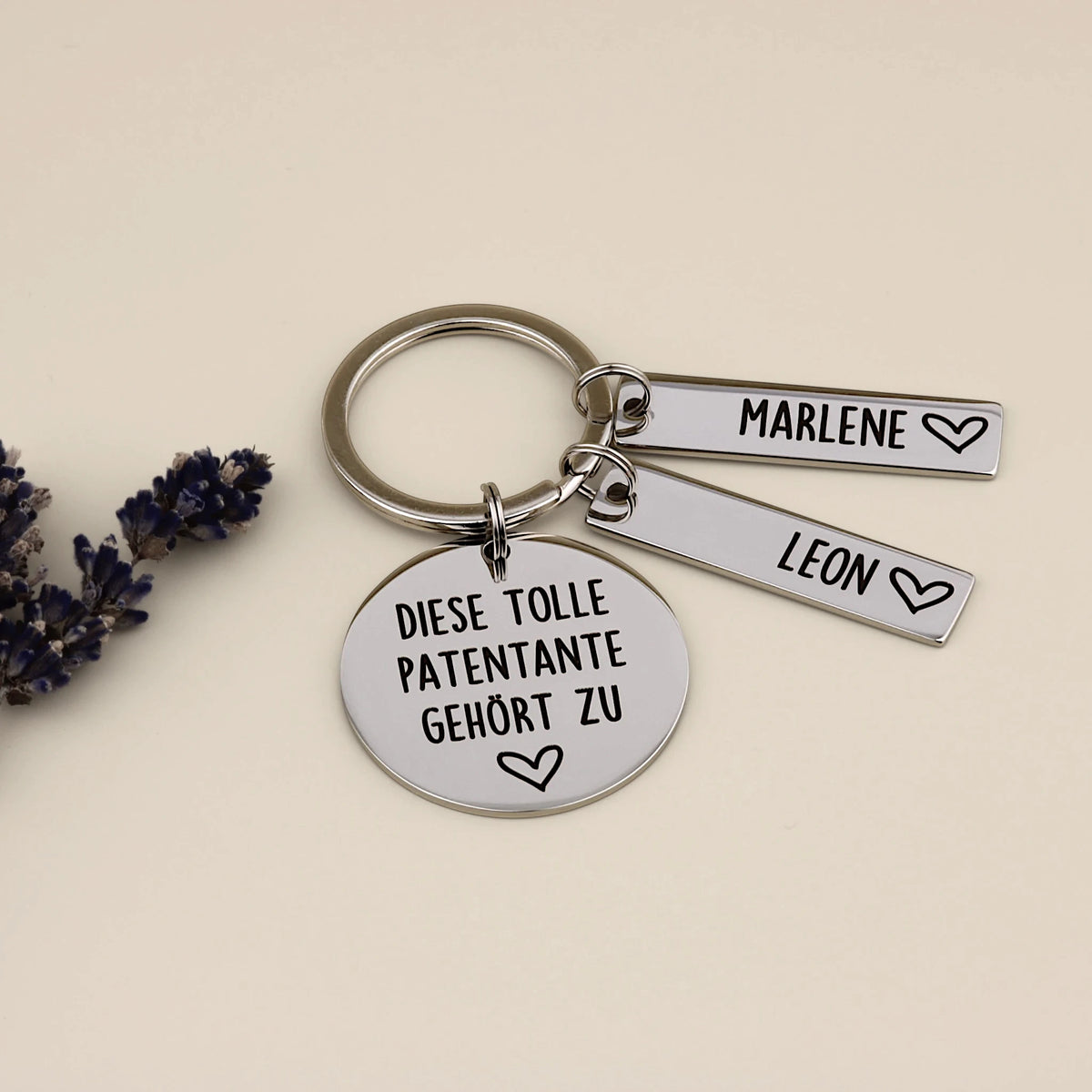 Schlüsselanhänger „Diese tolle Patentante gehört zu“ mit zwei Namensanhängern neben Lavendel.