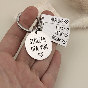 Person hält einen personalisierten Stolzer Opa-Schlüsselanhänger mit vier Namensanhängern als Größenvergleich.