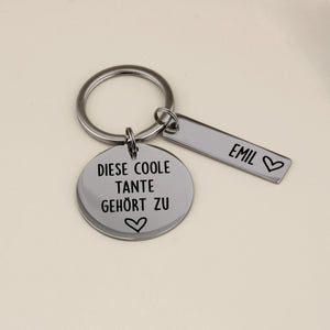 Nahaufnahme des gravierten Schlüsselanhängers 'Diese coole Tante gehört zu' mit einem Namensanhänger für Emil.