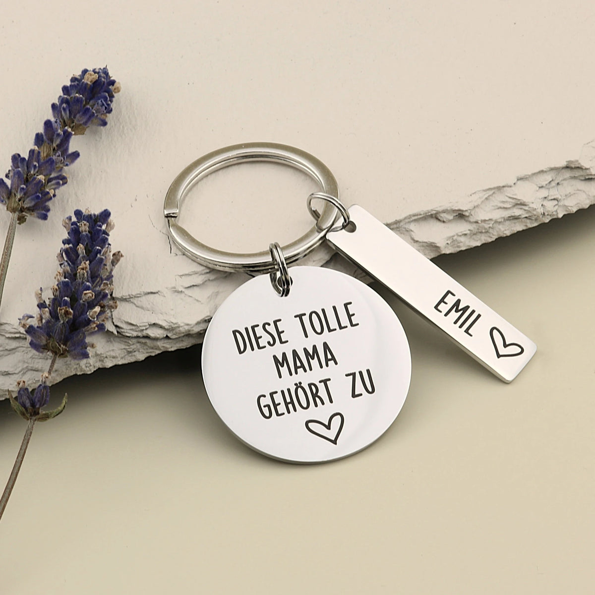 Tolle-Mama-Schlüsselanhänger „Diese tolle Mama gehört zu“ mit Namensanhänger Emil neben Lavendel