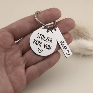 Schlüsselanhänger „Stolzer Papa von“ mit Namensanhänger Oskar in einer Hand als Größenvergleich.