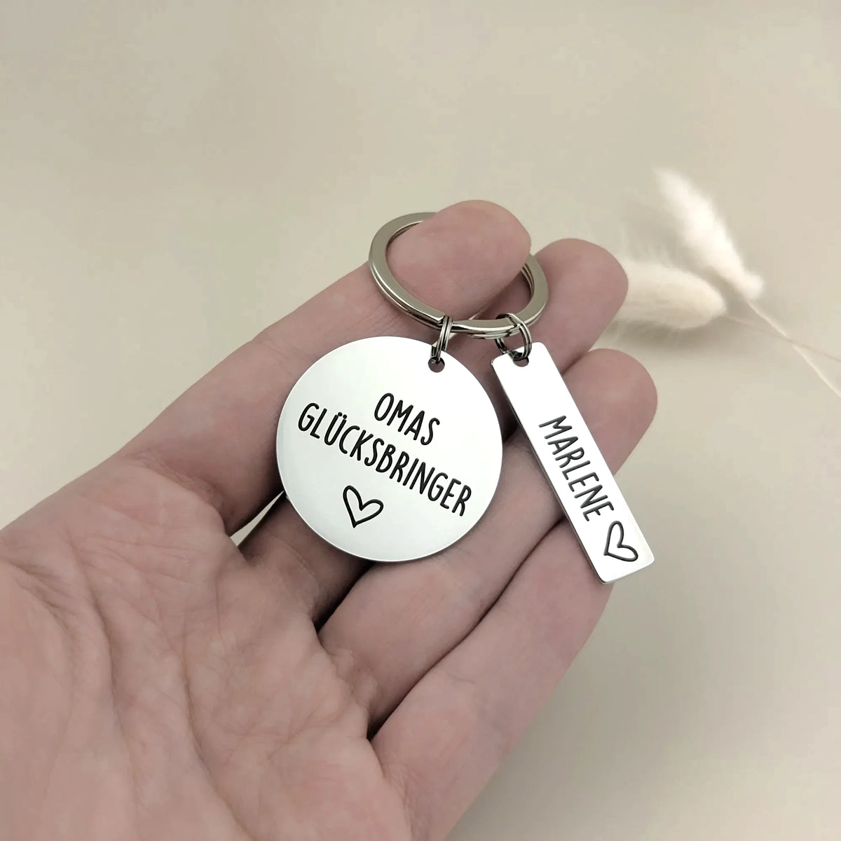 Größenvergleich von Omas Glücksbringer Schlüsselanhänger mit einem Namensanhänger in der Hand