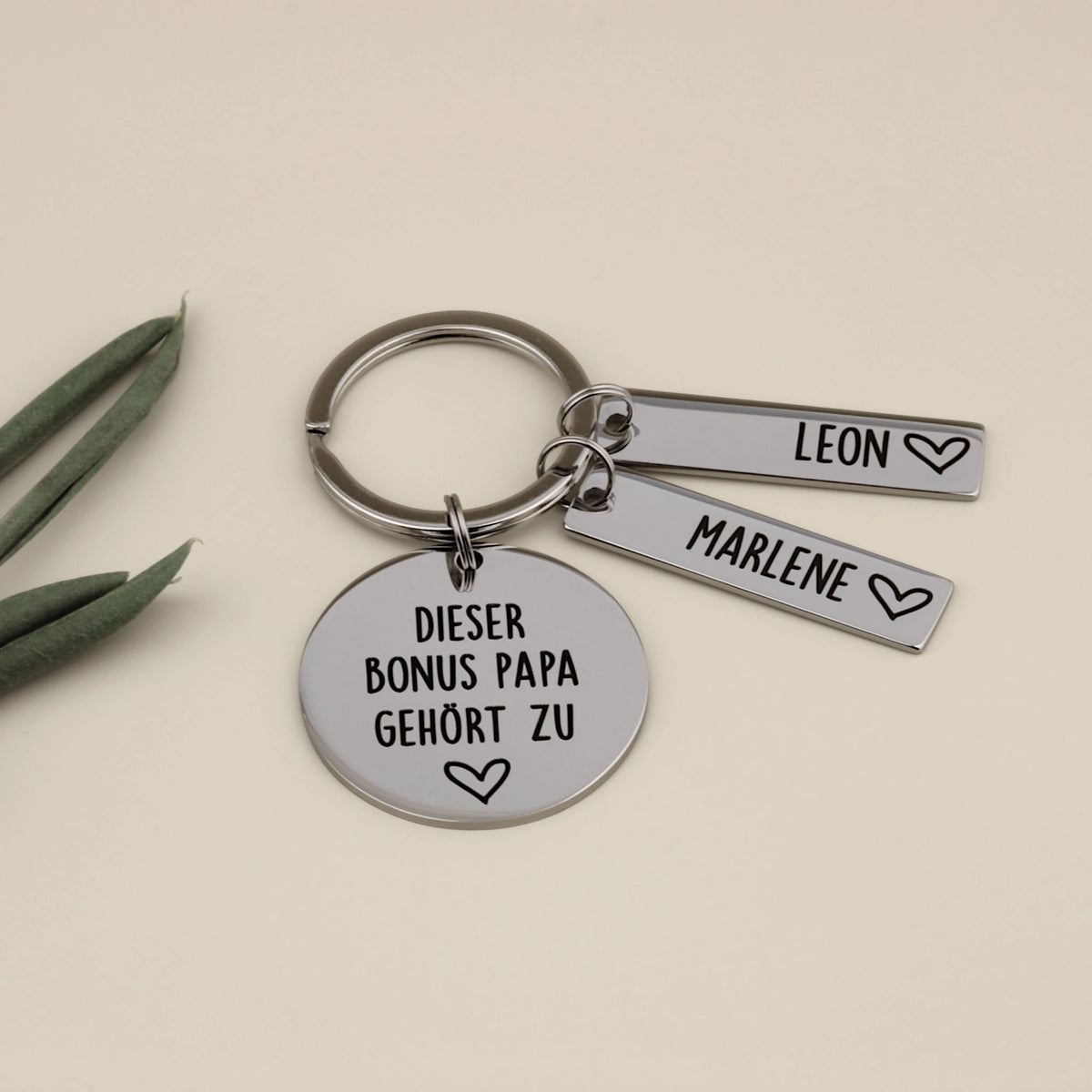 Schlüsselanhänger für den Bonus Papa aus Edelstahl mit zwei Namensanhängern für Leon und Marlene, liebevoll dekoriert.
