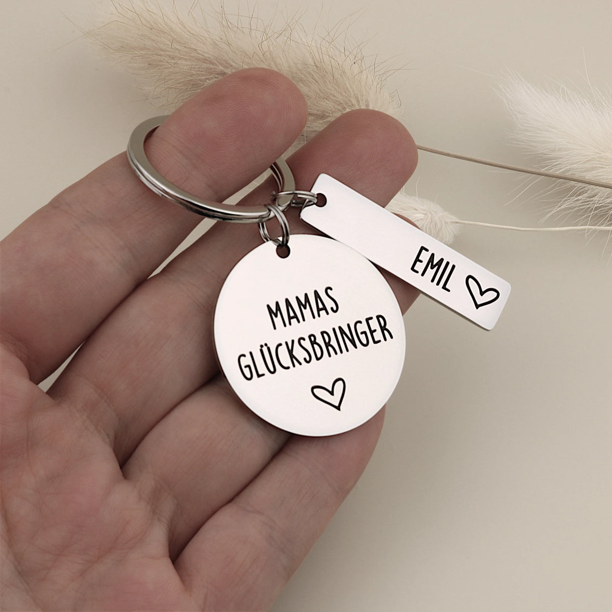 Mamas-Glücksbringer-Schlüsselanhänger mit Namensanhänger Emil als Größenvergleich in einer Hand.
