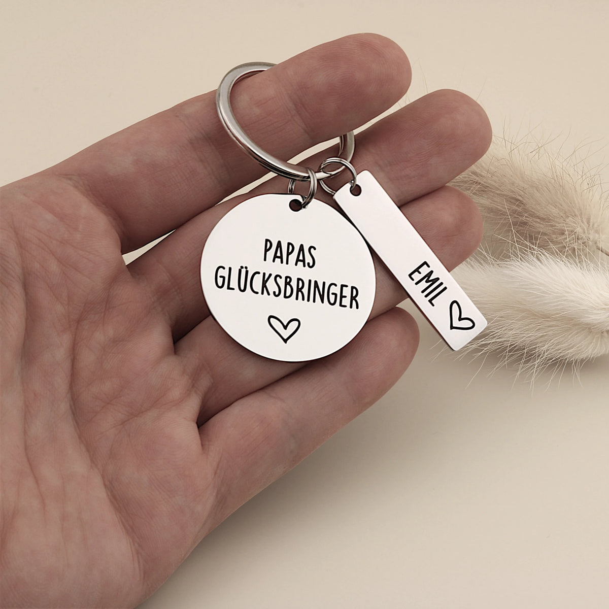 Papas Glücksbringer Schlüsselanhänger mit Namensanhänger in einer Hand als Größenvergleich.
