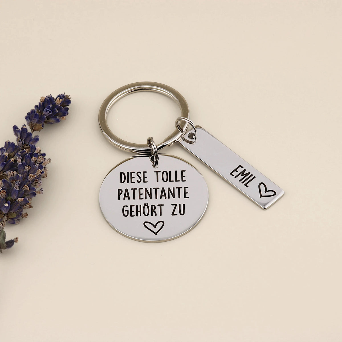 Schlüsselanhänger „Diese tolle Patentante gehört zu“ mit Namensanhänger Emil neben Lavendel.