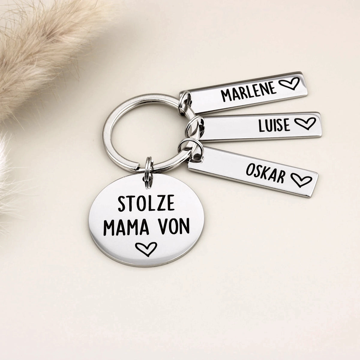 Schlüsselanhänger „Stolze Mama von“ mit Marlene, Luise und Oskar neben heller Dekoration.