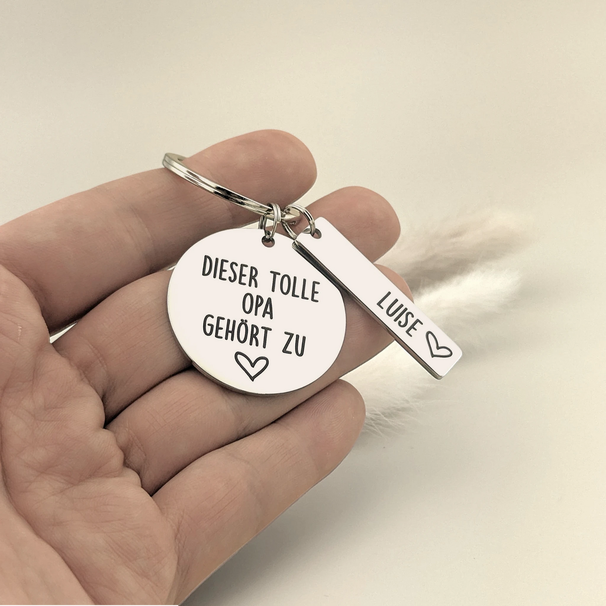 Hand hält den Schlüsselanhänger „Dieser tolle Opa gehört zu“ mit Namensanhänger Luise.