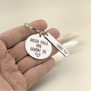 Hand hält den Schlüsselanhänger „Dieser tolle Opa gehört zu“ mit Namensanhänger Luise.