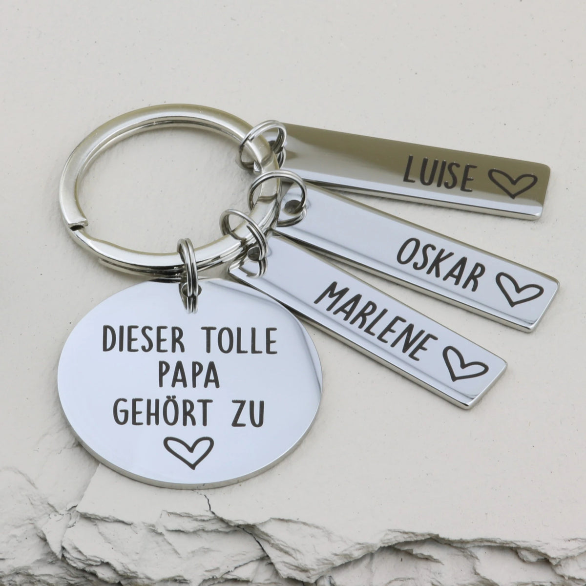 Schlüsselanhänger „Dieser tolle Papa gehört zu“ mit drei Namensanhängern Luise, Oskar und Marlene.