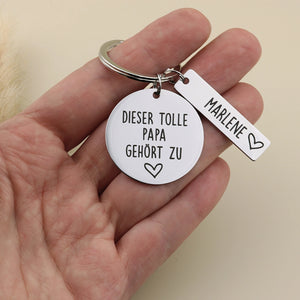Hand hält den Schlüsselanhänger „Dieser tolle Papa gehört zu“ mit Namensanhänger Marlene.