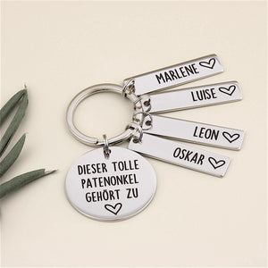 Schlüsselanhänger „Dieser tolle Patenonkel gehört zu“ mit vier Namensanhängern und grüner Dekoration.