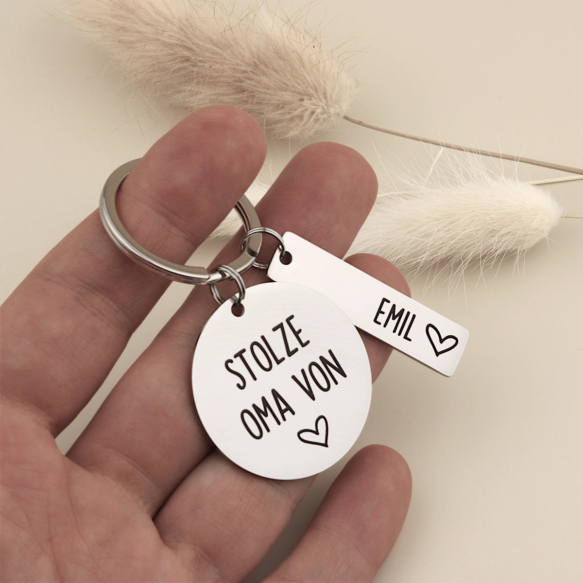 Personalisierter Stolze-Oma-Schlüsselanhänger mit Namensanhänger Emil in einer Hand als Größenvergleich.